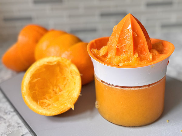 Citrus juicer filled with orange juice and empty orange halves on the side.