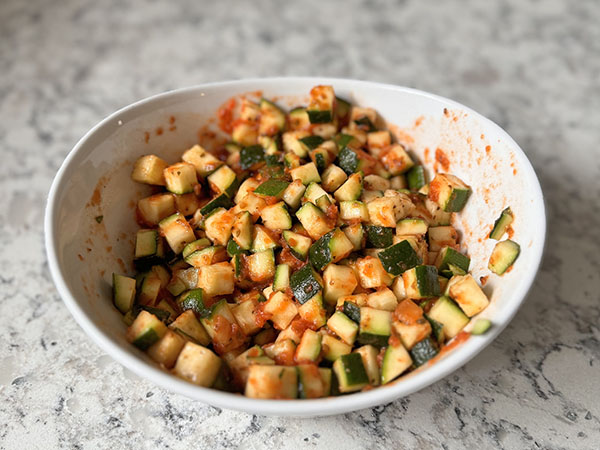 A bowl of fresh zucchini cubes mixed with marinara and seasoned with oregano.