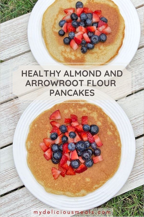 Two plates of arrowroot starch and almond flour pancakes topped with a colorful mixture of strawberries and blueberries.