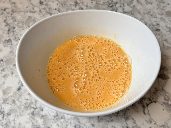 Wet ingredients for apple donut pancakes whisked in a bowl.