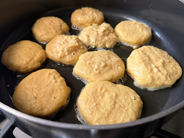 Apple donut pancakes frying in a skillet.