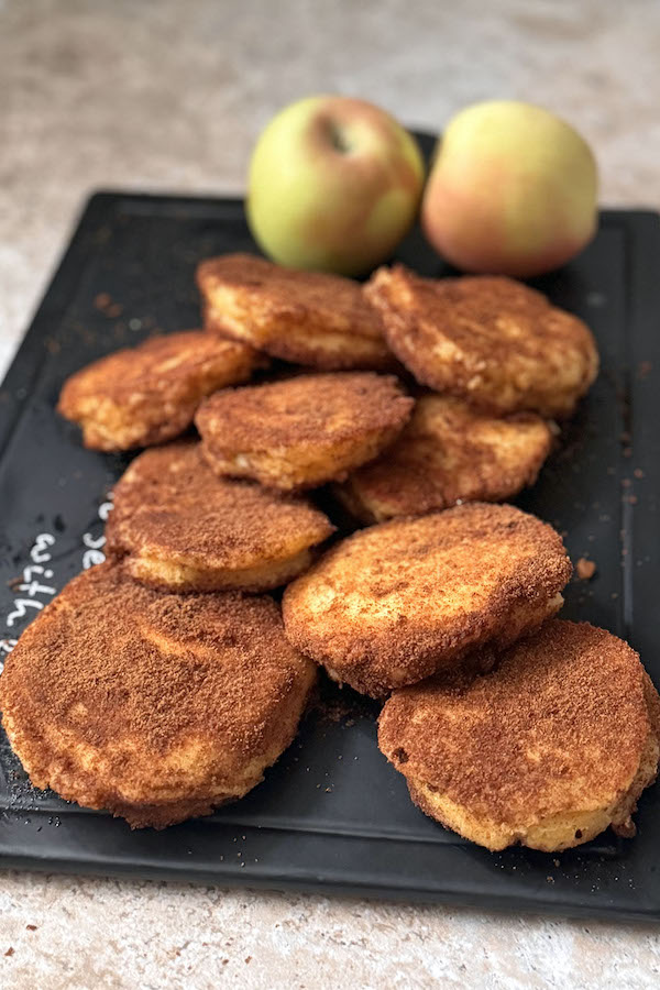 Apple cinnamon-sugar donut pancakes on a serving broad with fresh apples on the background.