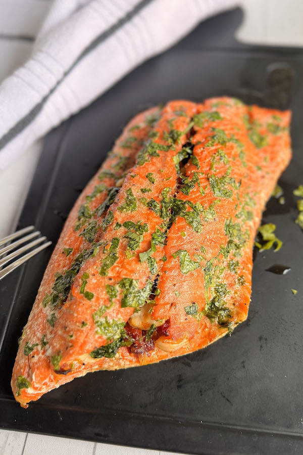 Baked salmon stuffed with Tuscan style shrimp on a serving board.
