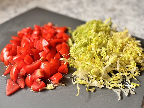 Shredded lettuce and chopped tomatoes on a cutting board.