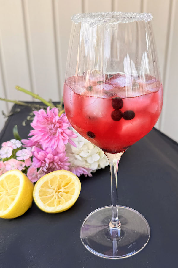 Blueberry Lemon Drop Martini Cocktail in a wine glass with fresh flowers and lemon in the background.