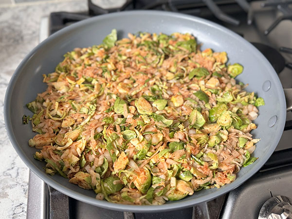 Potato and Brussels sprouts breakfast hash cooking in a skillet.