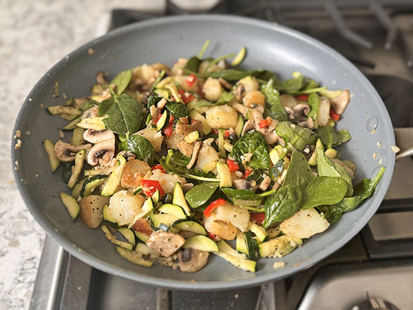 Potatoes, zucchini and mushrooms hash cooking in a skillet.
