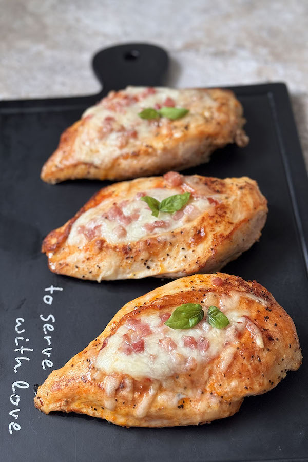 Baked stuffed chicken breasts on a serving board topped with basil.