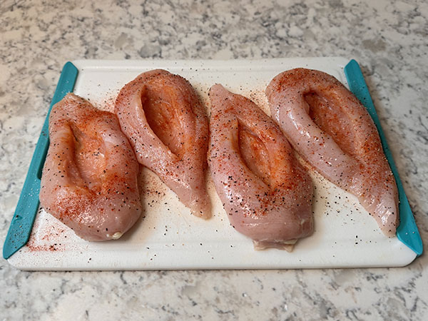 Raw seasoned chicken breasts with pockets cut for filling.