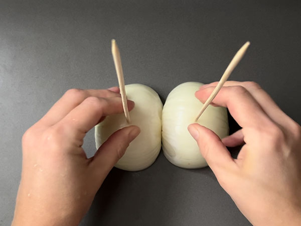 Self-made vertical spit for chicken stack made of skewers inserted into onion halves.