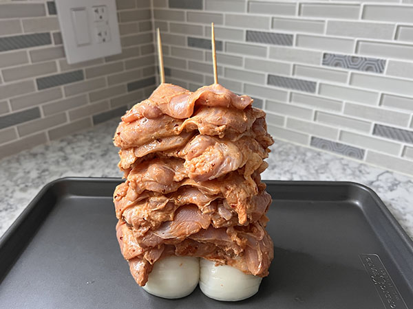 Chicken thighs stacked through skewers making chicken tower.