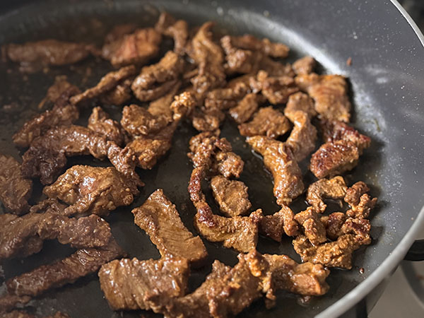 Golden brown beef shawarma searing on stovetop.