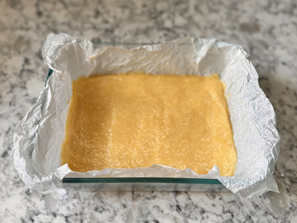 Coconut layer of the chocolate coconut bars pressed onto the bottom of a glass dish.