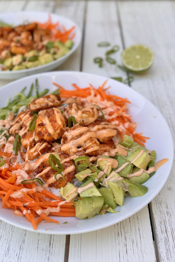 Два боула с креветками, рисом, морковкой, огурцом, авокадо и зелёным луком, политые пикантным соусом.