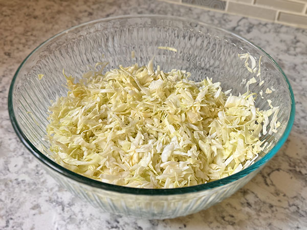 Shredded cabbage in a bowl, slightly massaged with hands to soften.