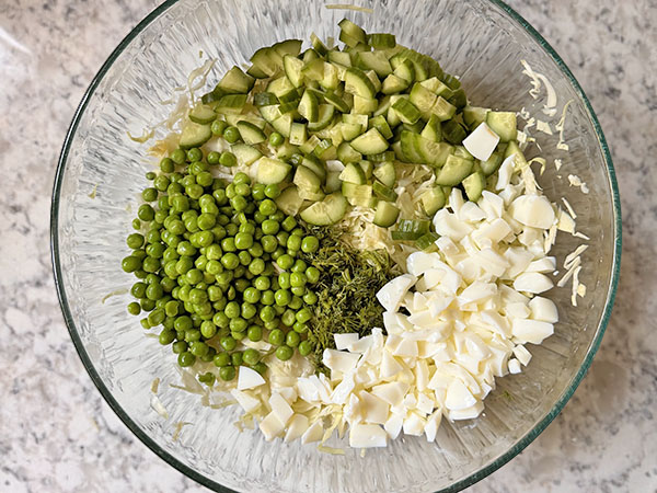 Ingredients for the cabbage salad in a bowl: cucumbers, pease, egg whites and dill sitting on top of cabbage.