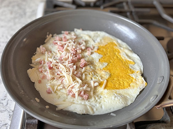 Christmas tree omelette with added fillings: pancetta and mozzarella cheese, cooking on the stove top.