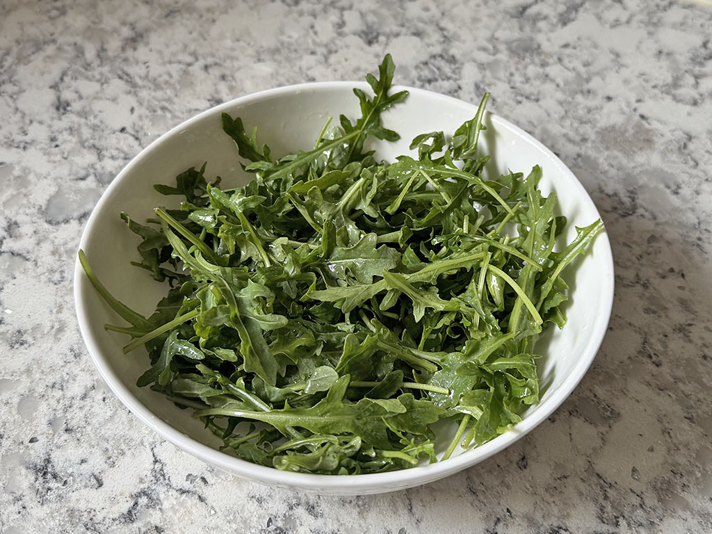 Arugula in a bowl tossed with lemon, olive oil and salt.