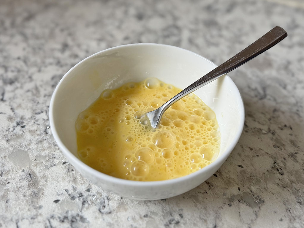 Eggs whisked with a fork in a small bowl.