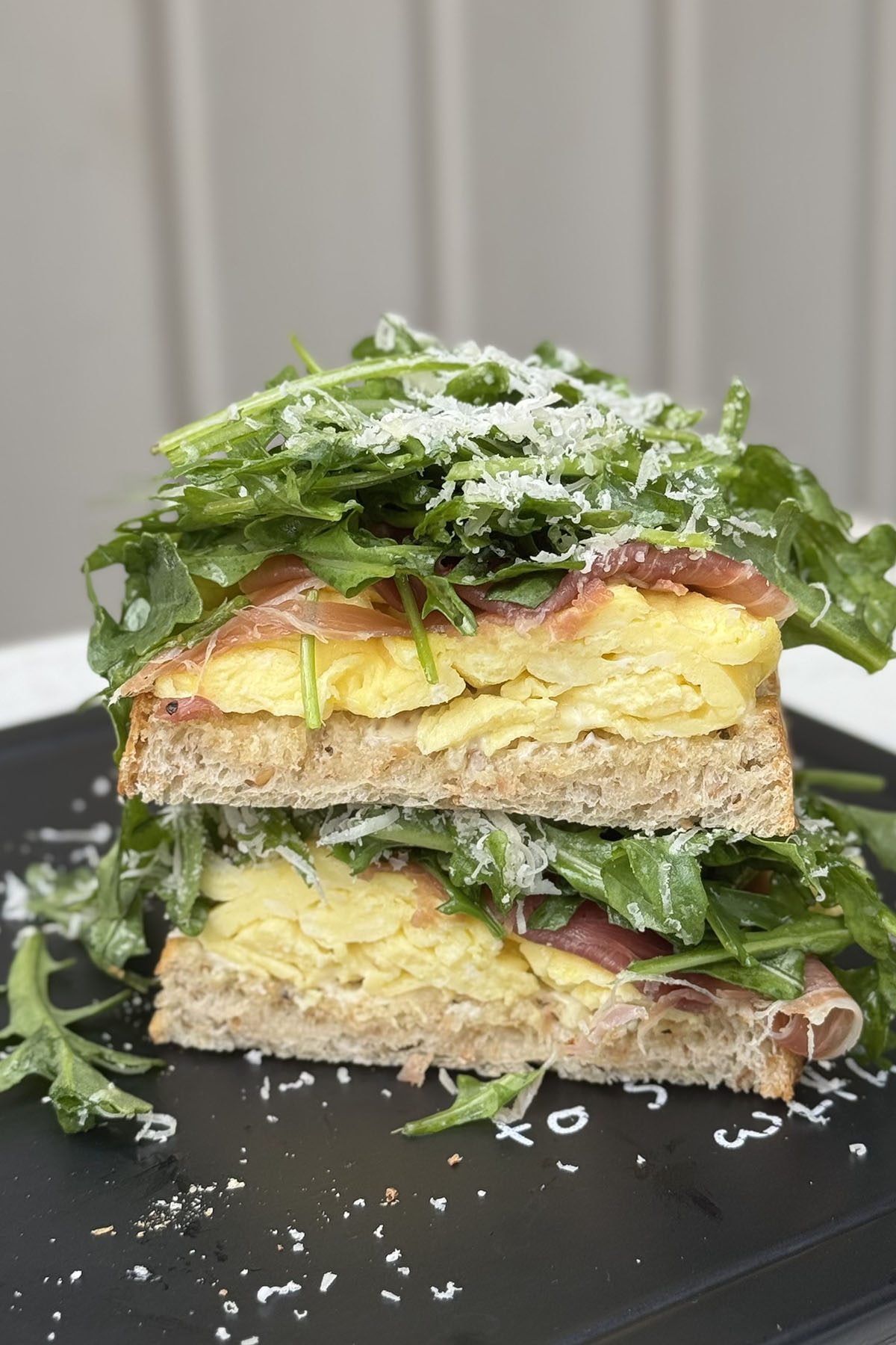 High protein arugula and prosciutto breakfast sandwich cut in half on a serving board.