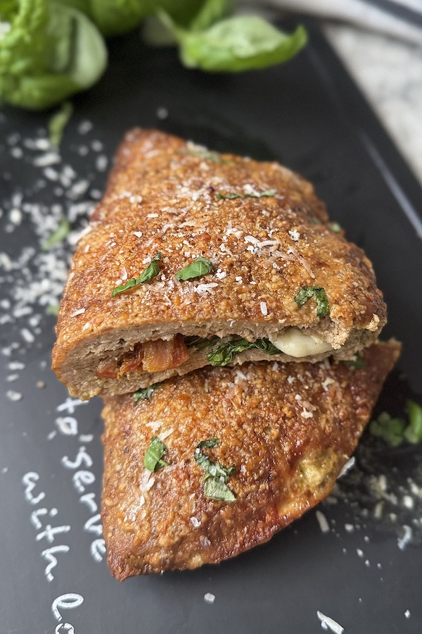 Hot turkey pocket topped with basil and cut in half with exposed mozzarella, spinach and sun-dried tomatoes filling.
