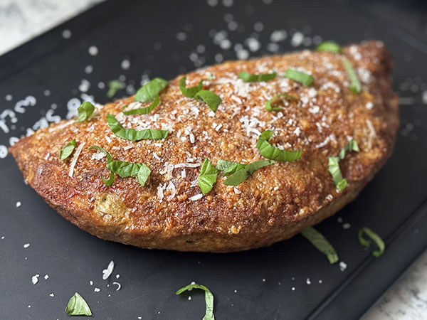 Baked hot turkey pocket topped with sliced basil leaves on a cutting board.