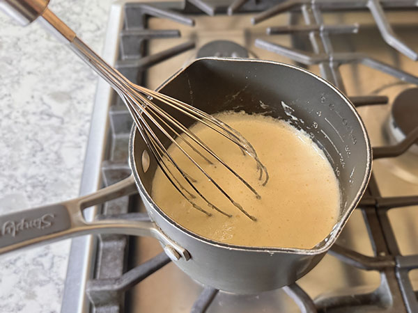 Заварной крем в кастрюле с венчиком на плите.
