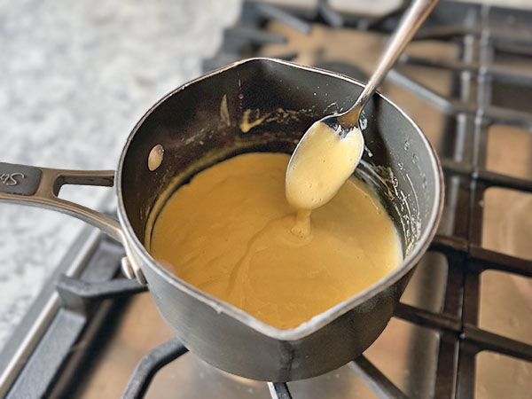 Густой заварной крем, зачерпнутый ложкой и образующий дорожку, которая показывает его консистенцию.