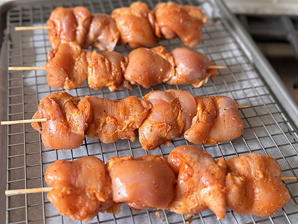 Marinated chicken thighs threaded onto bamboo skewers ready for cooking.