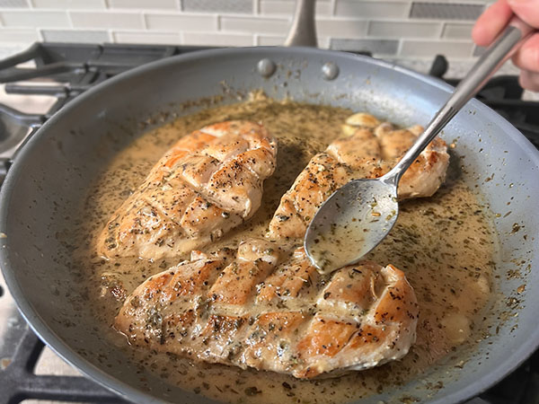 Golden brown chicken breasts in a skillet with lemon-mustard sauce spooned over.
