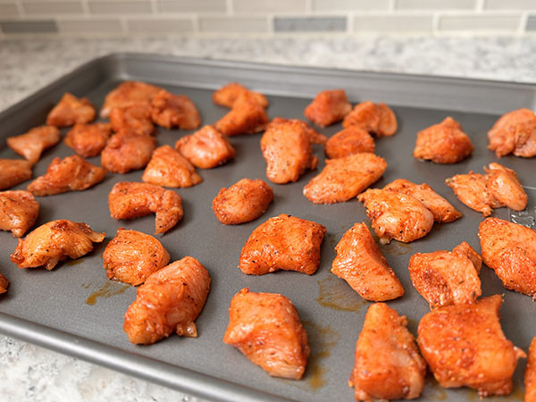 Seasoned pieces of chicken breasts on a baking sheet, ready for oven.