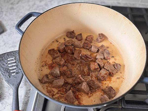 Pieces of beef searing in a Dutch oven.