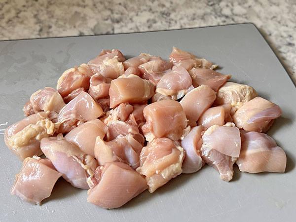 Chicken thighs cut into bite-sized cubes on a cutting board.