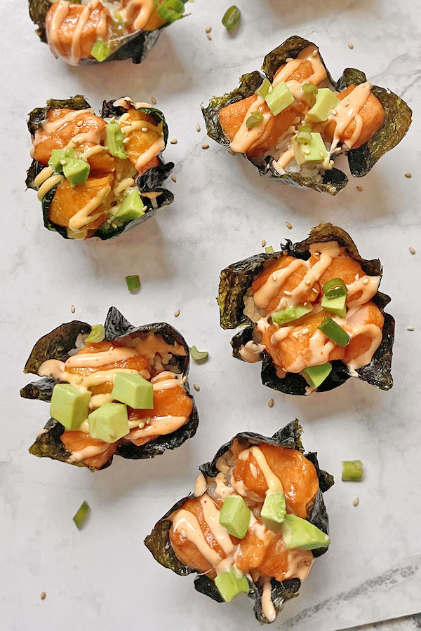 Spicy salmon sushi bites on a serving tray with scallion pieces and sesame seeds around them.