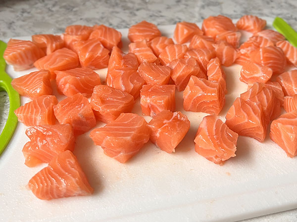 Fresh salmon cut into bite-sized pieces on a cutting board.