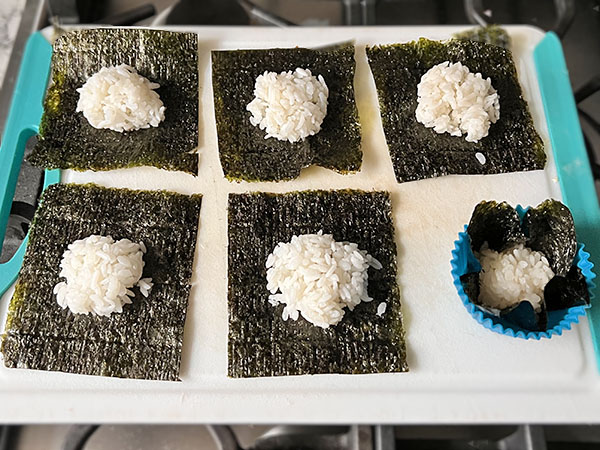 Nori squares with a spoon of rice on top, on a cutting board.