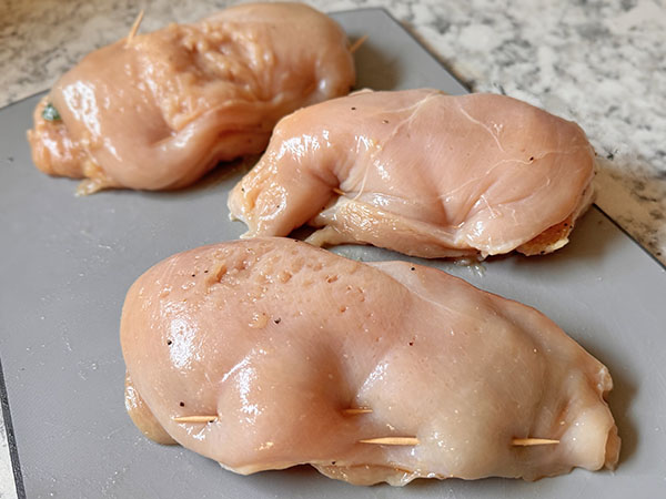 Stuffed chicken breasts secured with toothpicks on a cutting board.