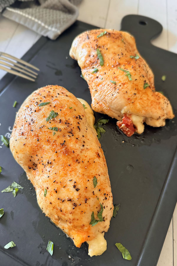 Baked chicken stuffed with spinach, mozzarella & sun-dried tomatoes on a serving board